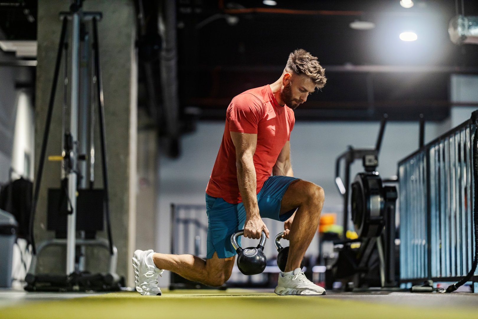 Profile view of powerful muscular masculine sportsman doing lunges with kettlebells at gym during strength training.