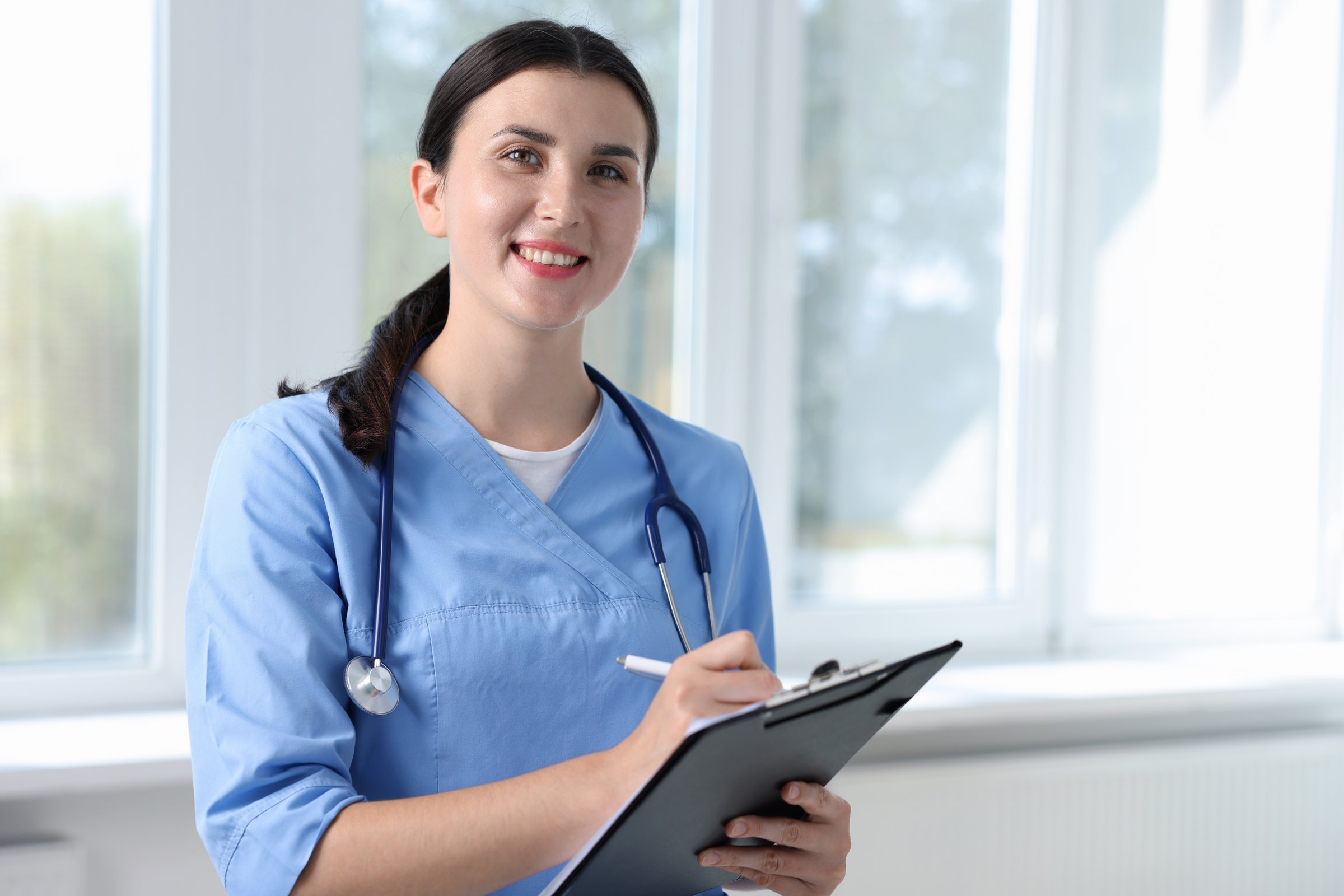 Nurse with clipboard taking notes near window in clinic, space for text