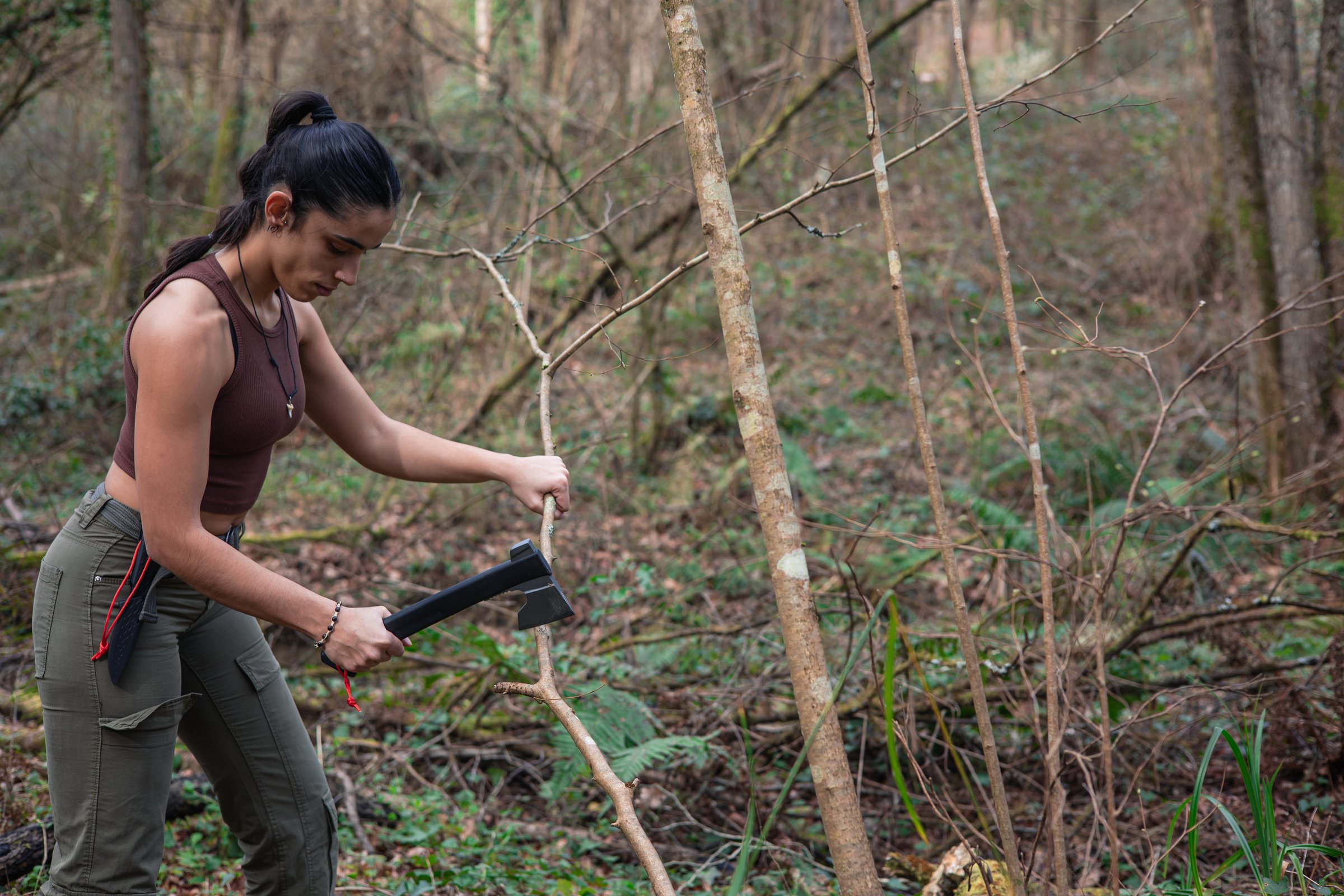 In this compelling image, a fearless adventurer undertakes the task of constructing a shelter in the heart of the forest, using bushcraft and survival skills to chop branches from a tree with an axe. Her determination and expertise underscore the importance of preparedness and connection with nature in wilderness environments. This moment captures the essence of self-sufficiency and adaptability in seeking safety and comfort amidst the wilderness.