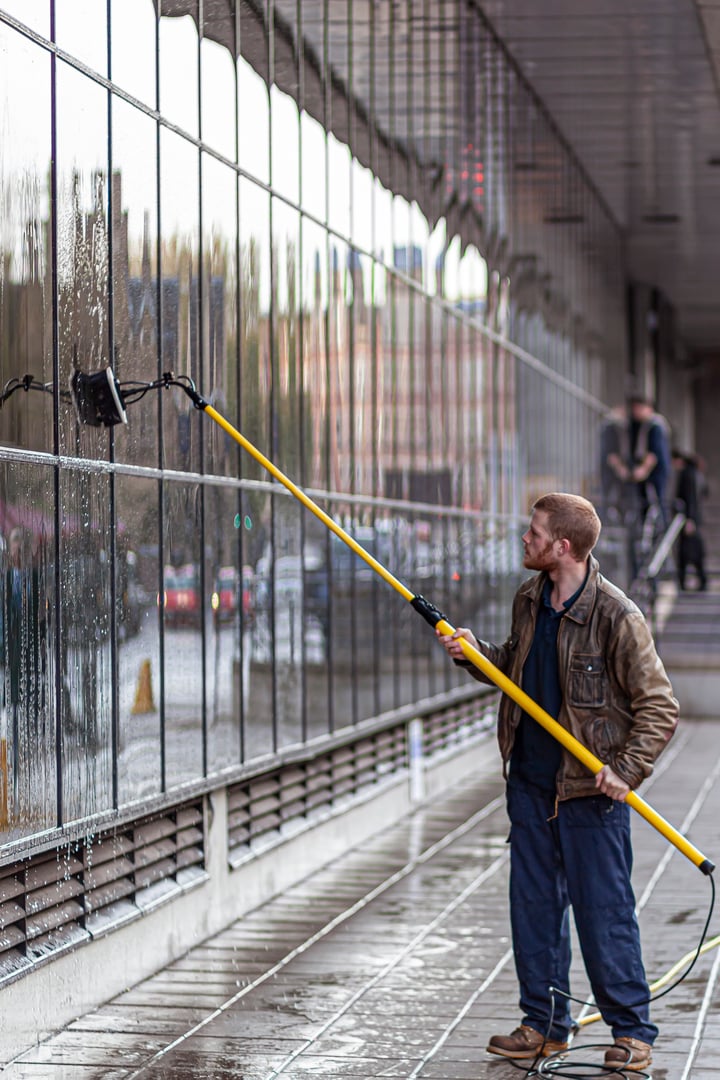 Oxford, UK, 12/09/2009: A caucasian man wearing boots, overalls and a leather jacket is cleaning the exterior windows of a building using a telescopic brush.