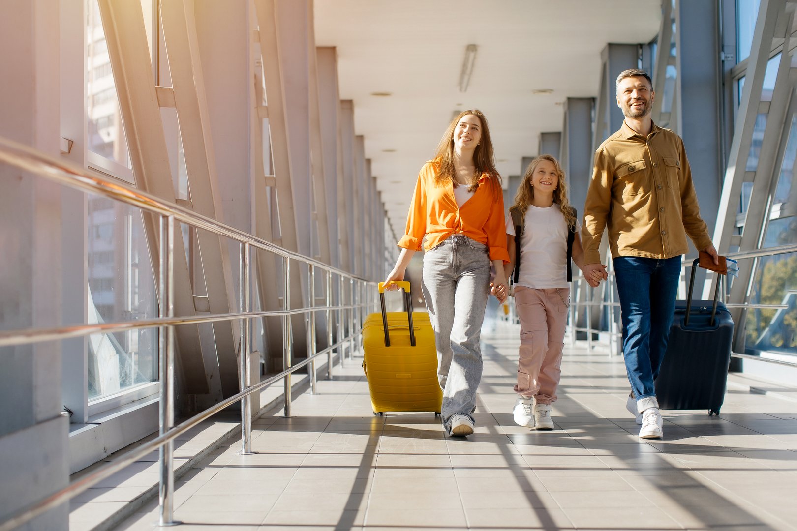 Caucasian family walking together at airport with luggage, holding hands and smiling in bright corridor, showing cheerful lifestyle, bonding and happy holiday travel