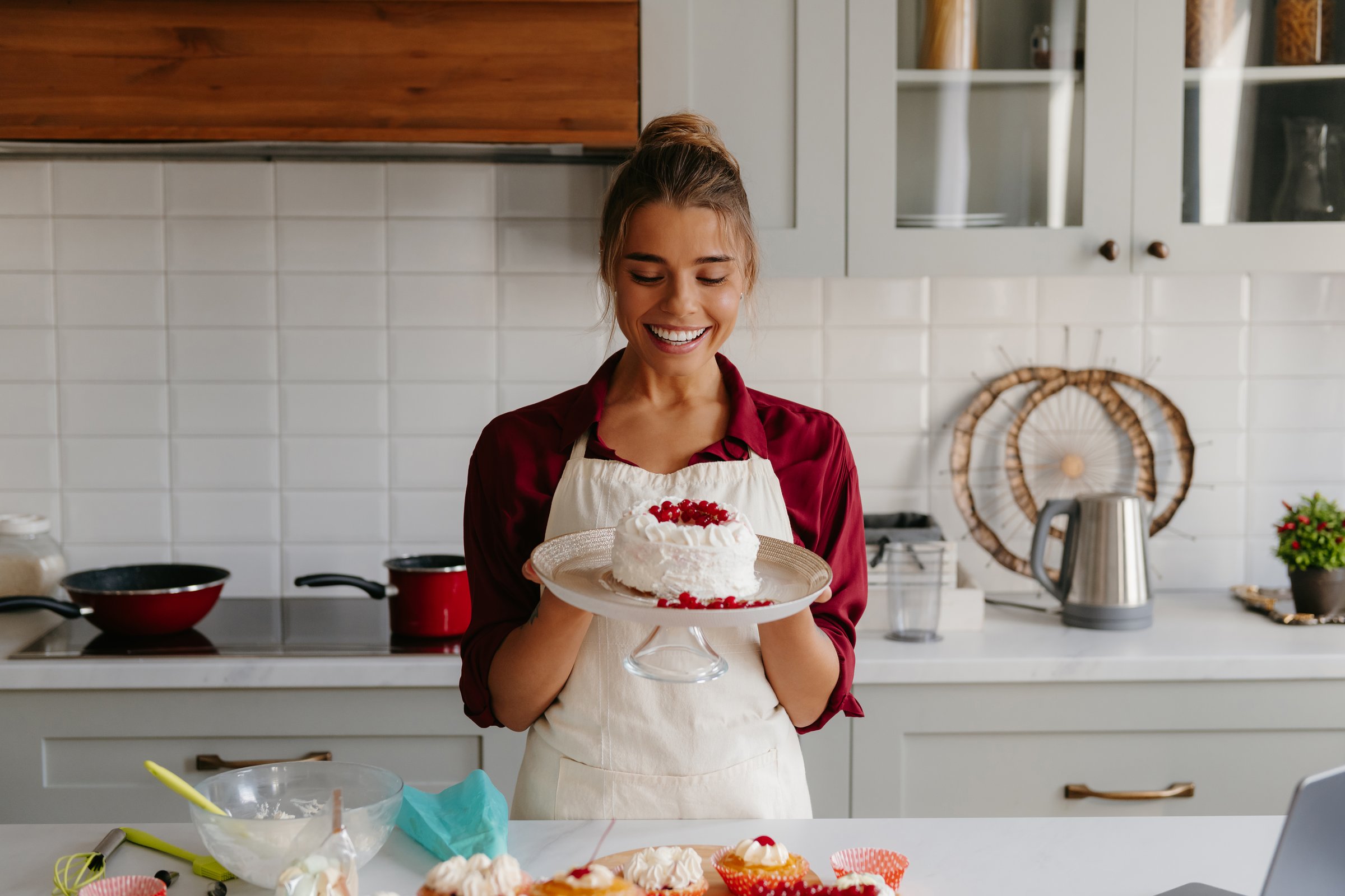 Happy female baker holding homemade cake and looking at it with smile while standing at the kitchen