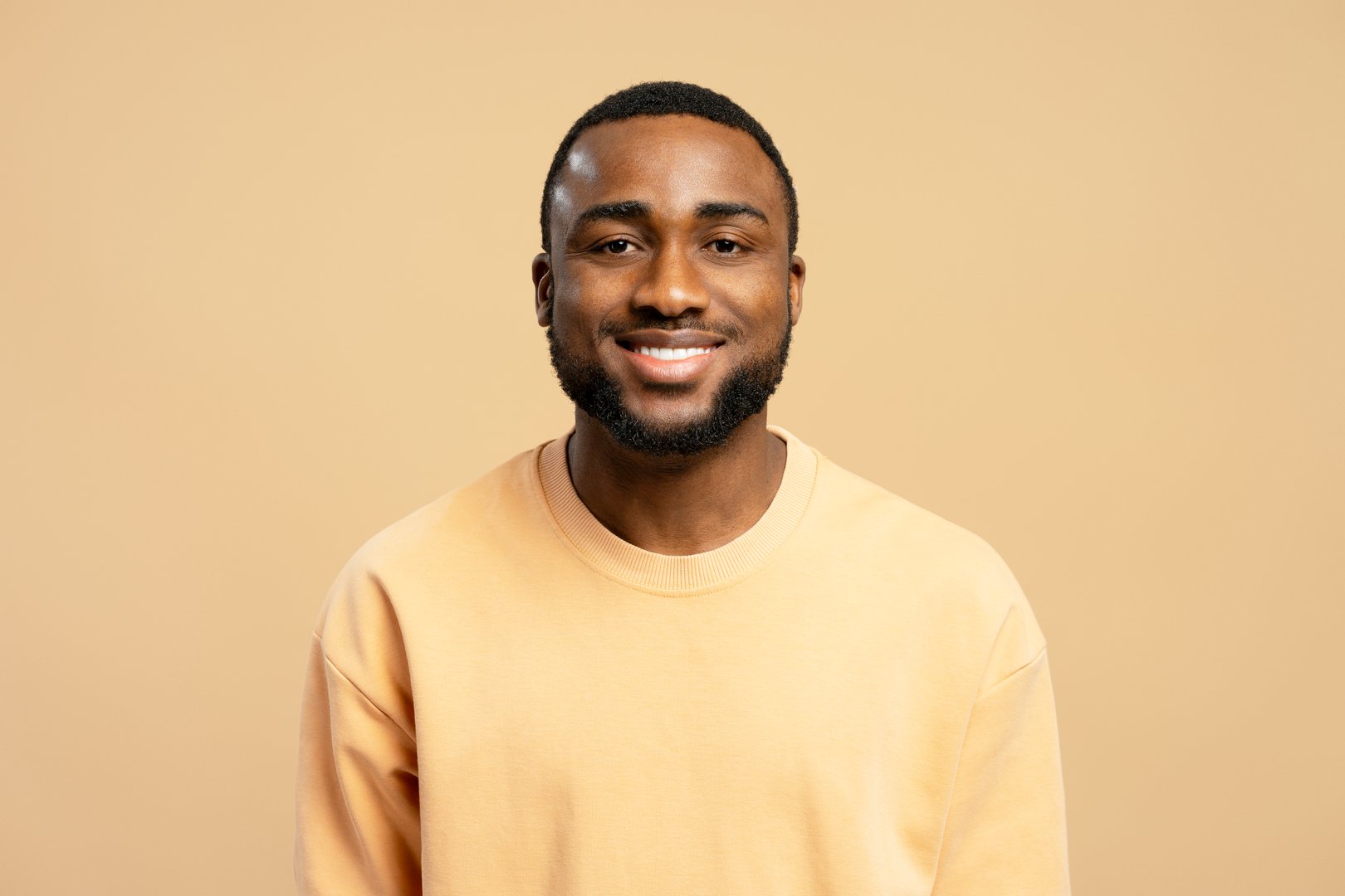 Portrait of smiling young african american man wearing casual beige sweatshirt posing on beige background