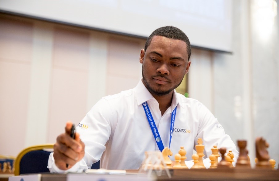 A person in a white shirt playing chess, focused on the game, holding a chess piece. The setting appears to be competitive.