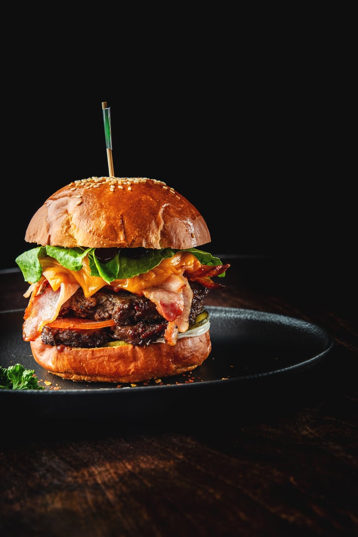 Delicious gourmet burger with layers of bacon, lettuce, and melted cheese, served on a sesame seed bun against a dark background
