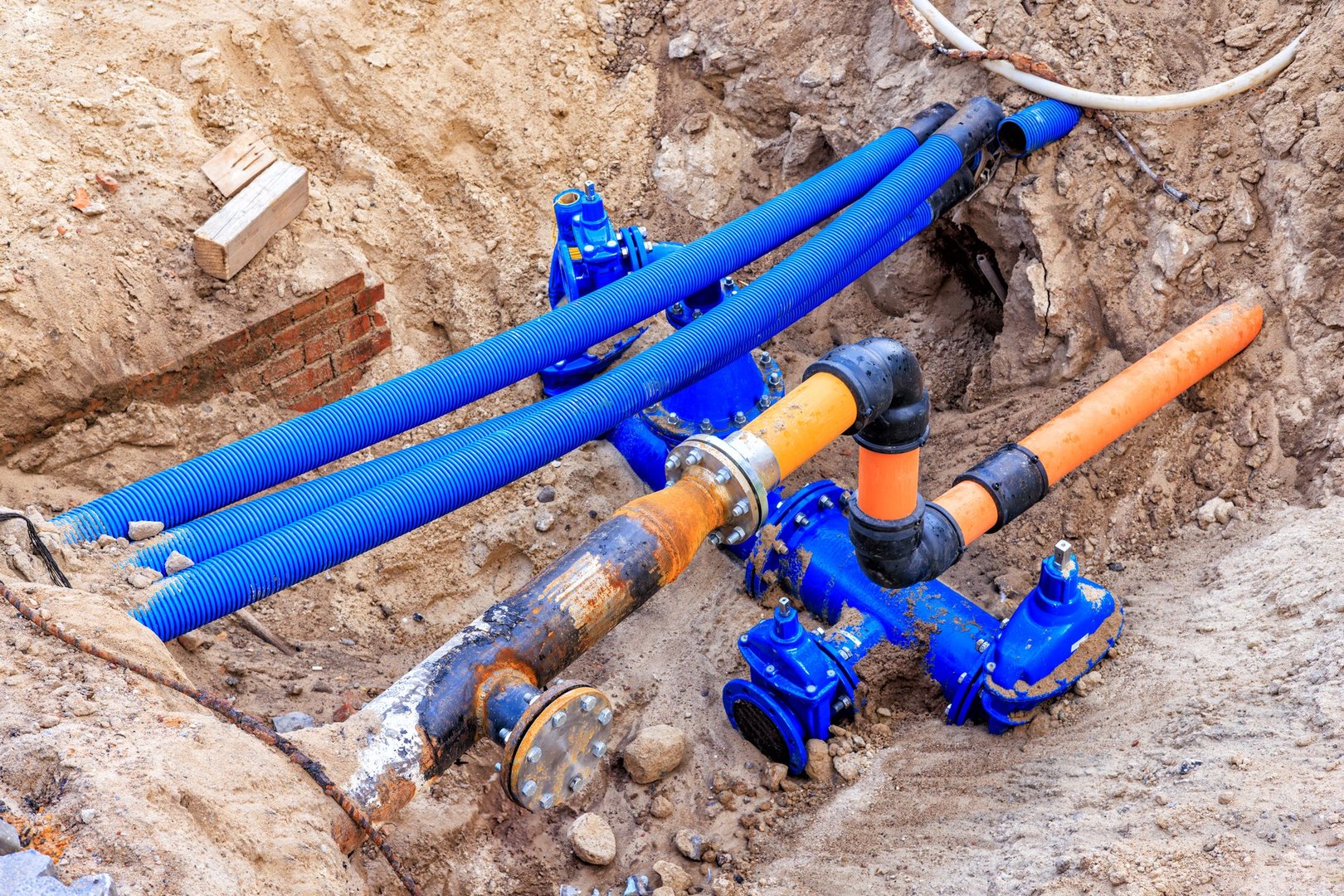 Blue and orange water pipes and cable conduits in a pit. Repair work is underway on city utilities