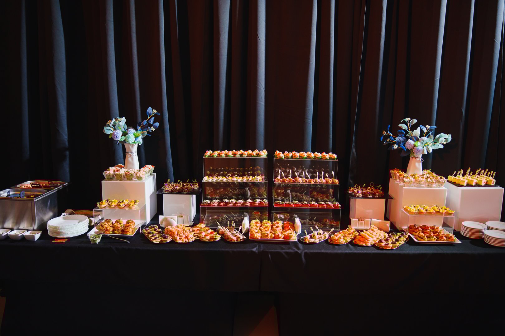 A beautifully arranged catering display features an assortment of gourmet appetizers and desserts on elegant tables.
