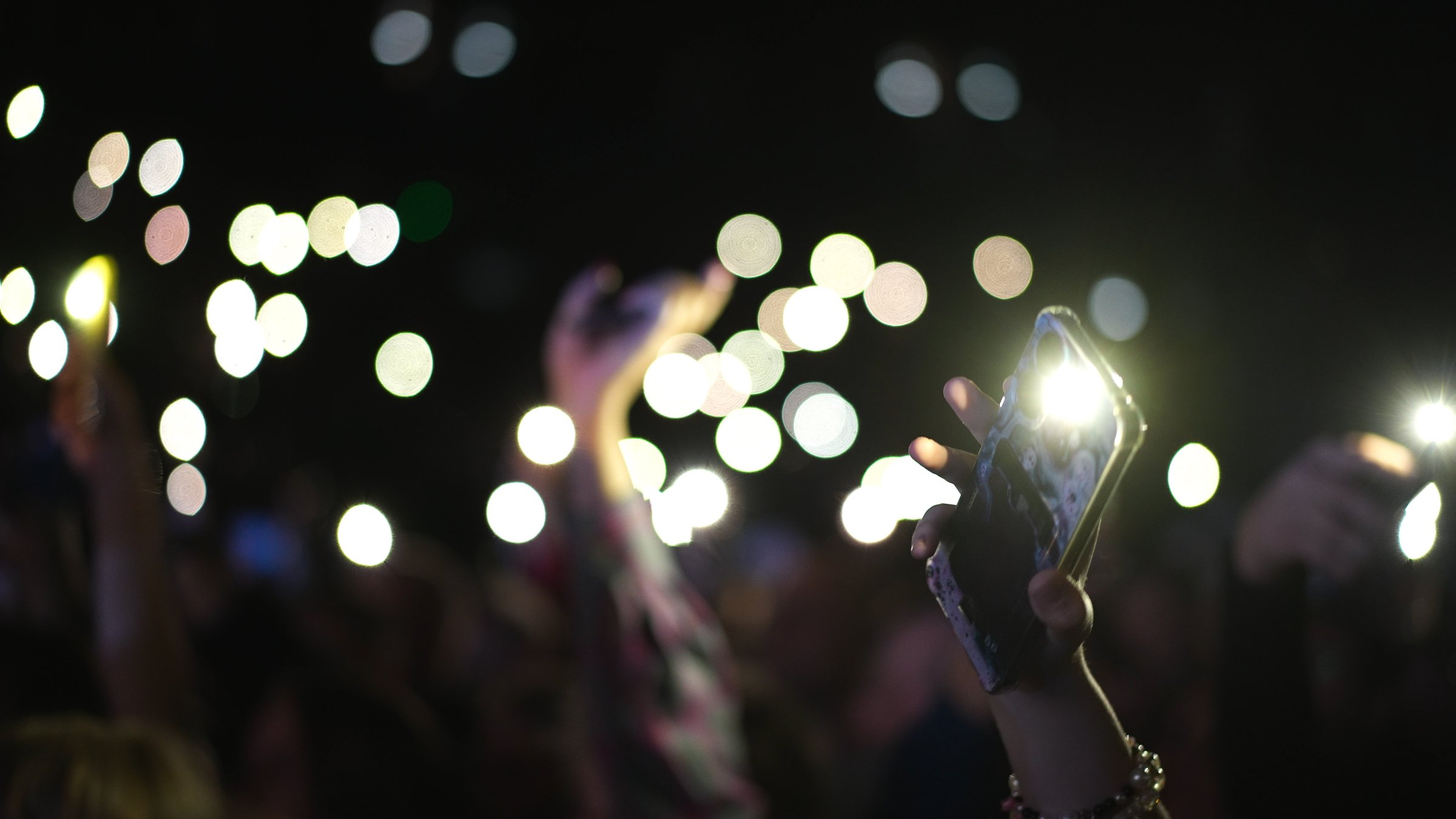 Many fun people lift hand up hold cell phone flash light. Fan crowd wave flashlights. Epic live music concert atmosphere. Big open air k pop arena. Cool night fest. Lot joy men hang out. Kpop chill.