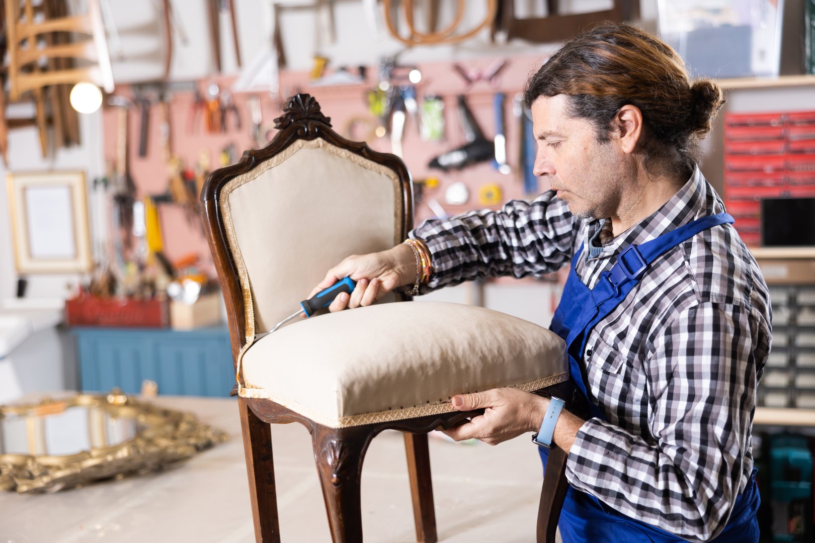 Skilled middle-aged male furniture repair specialist in uniform restoring Victorian chair during workday in workshop