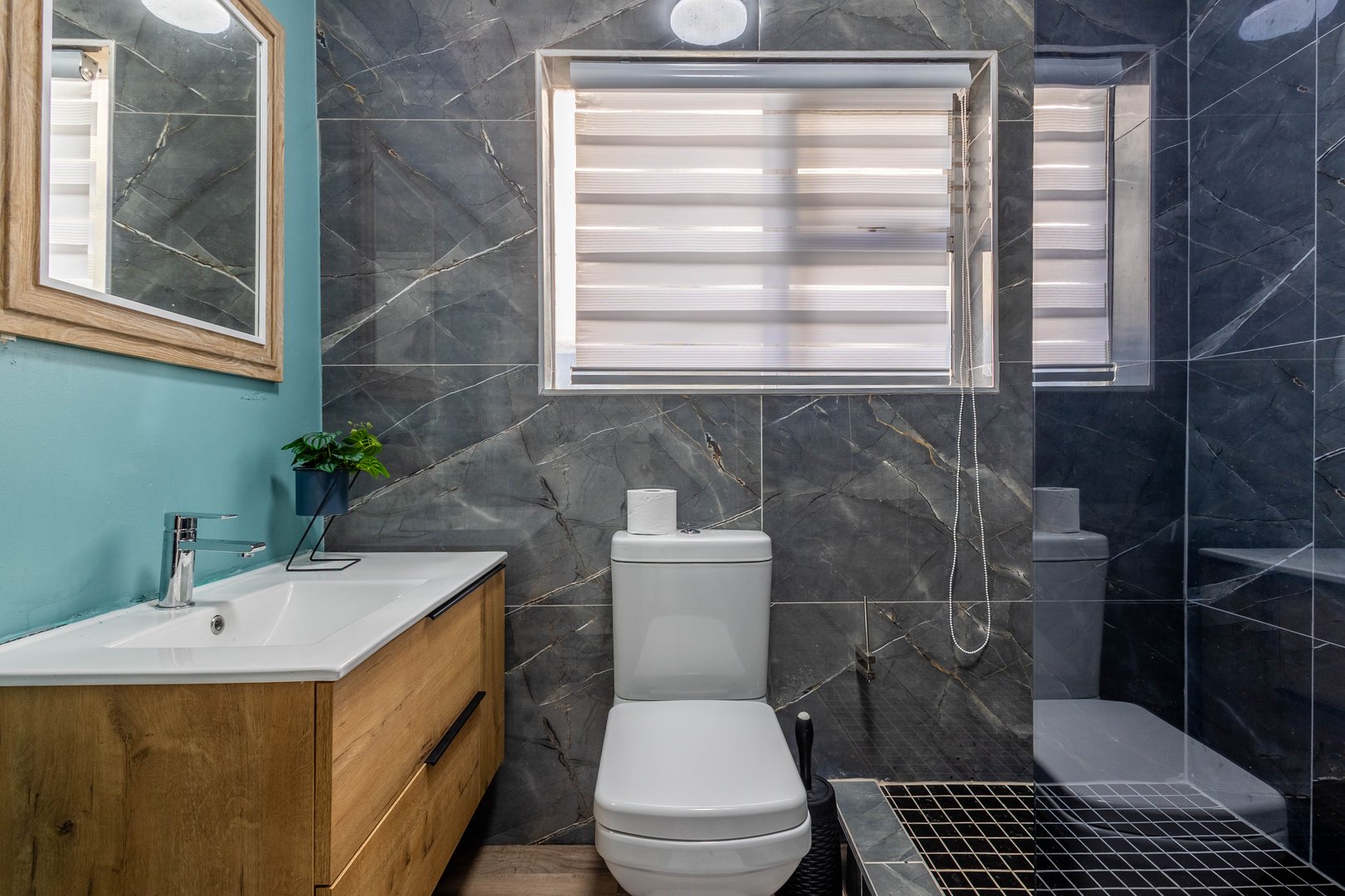 Modern bathroom with marble walls, a toilet, sink with cabinet, and a glass-enclosed shower.