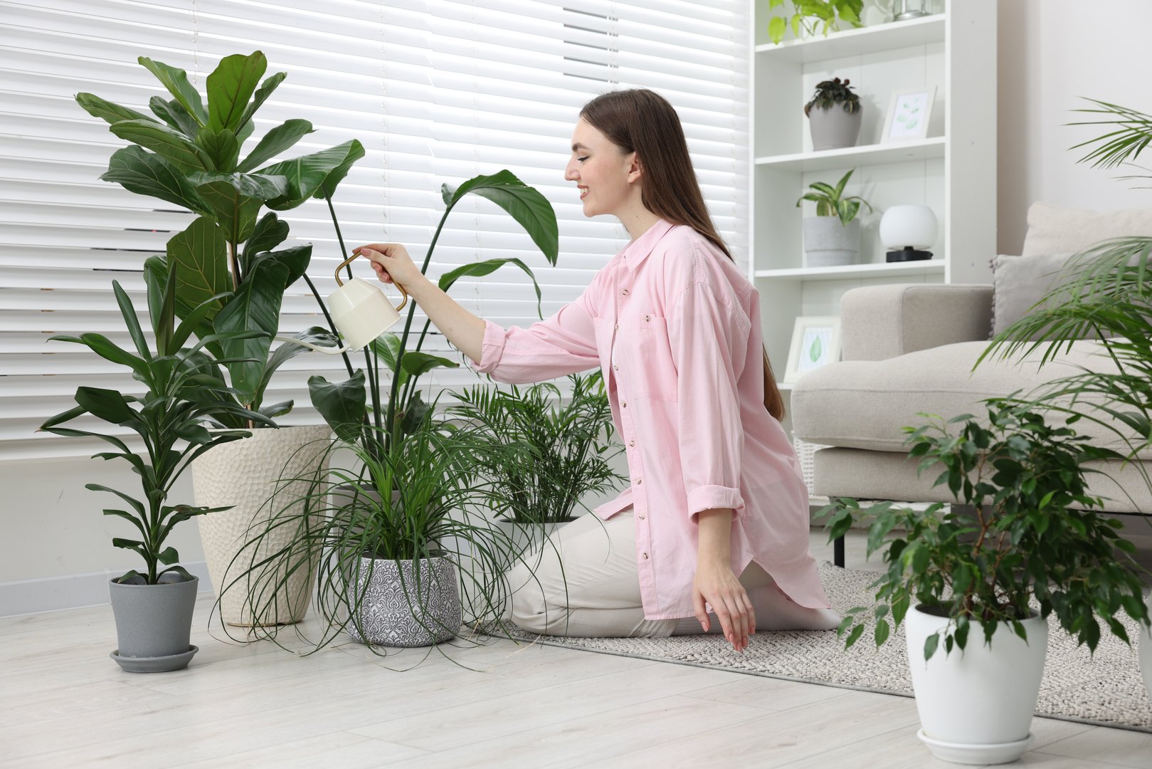 Beautiful young woman watering green houseplants at home