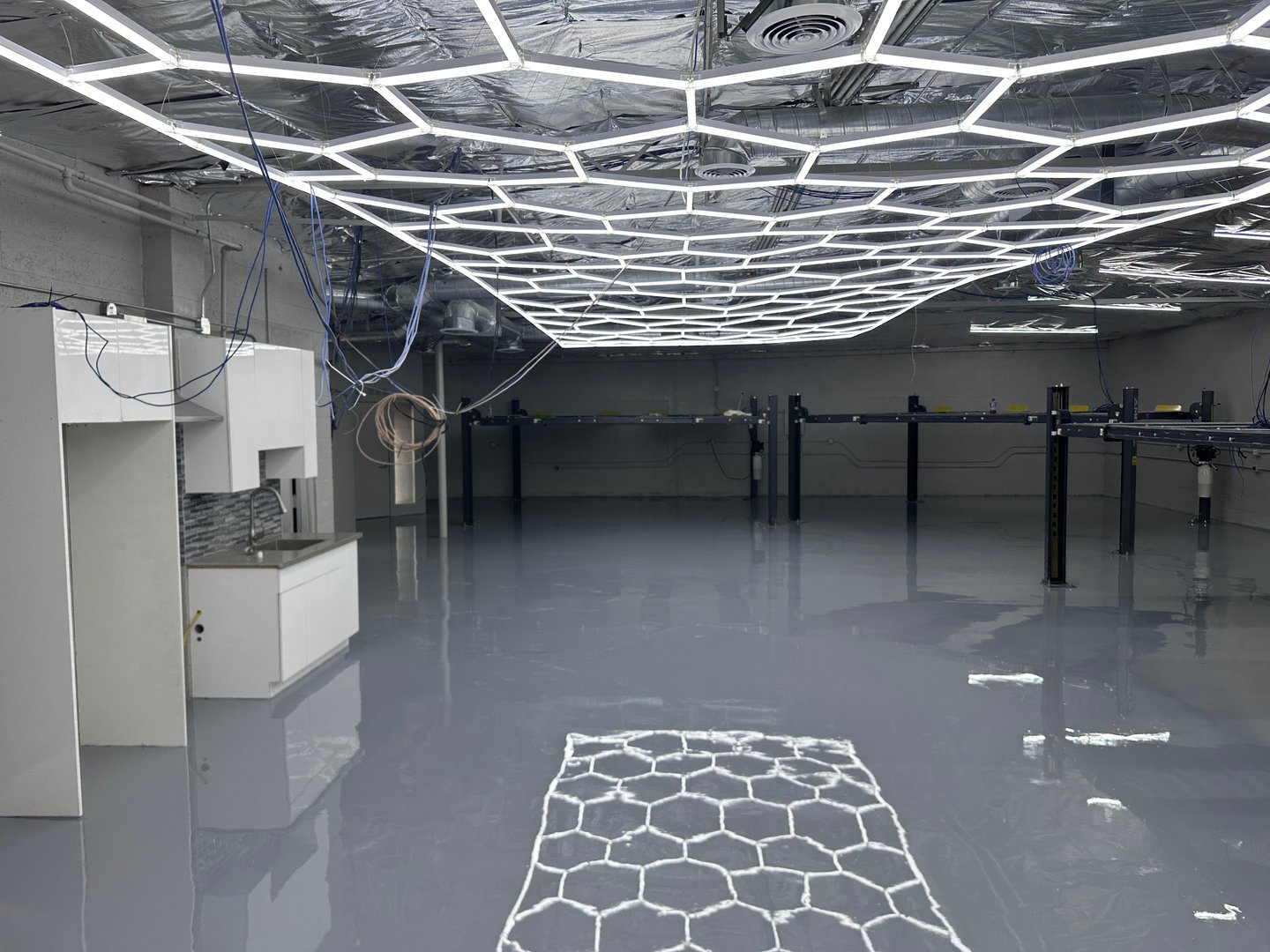 Modern industrial room with hexagonal LED ceiling lights, reflective floor, and exposed cables.