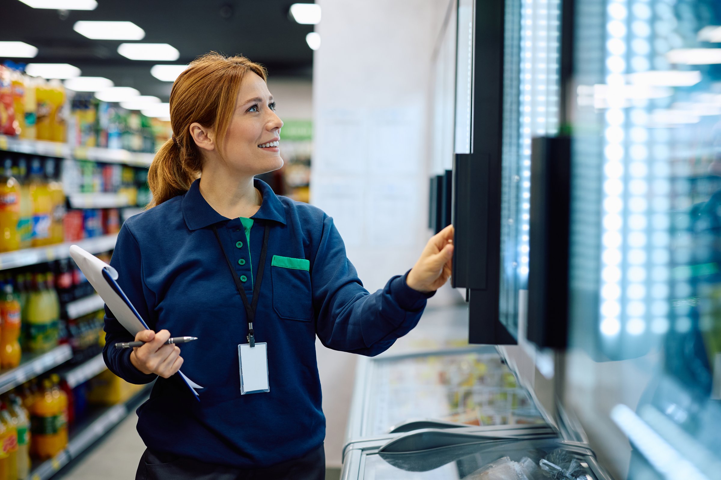 Happy female supermarket manager checking stock of products in refrigerated section. Copy space.