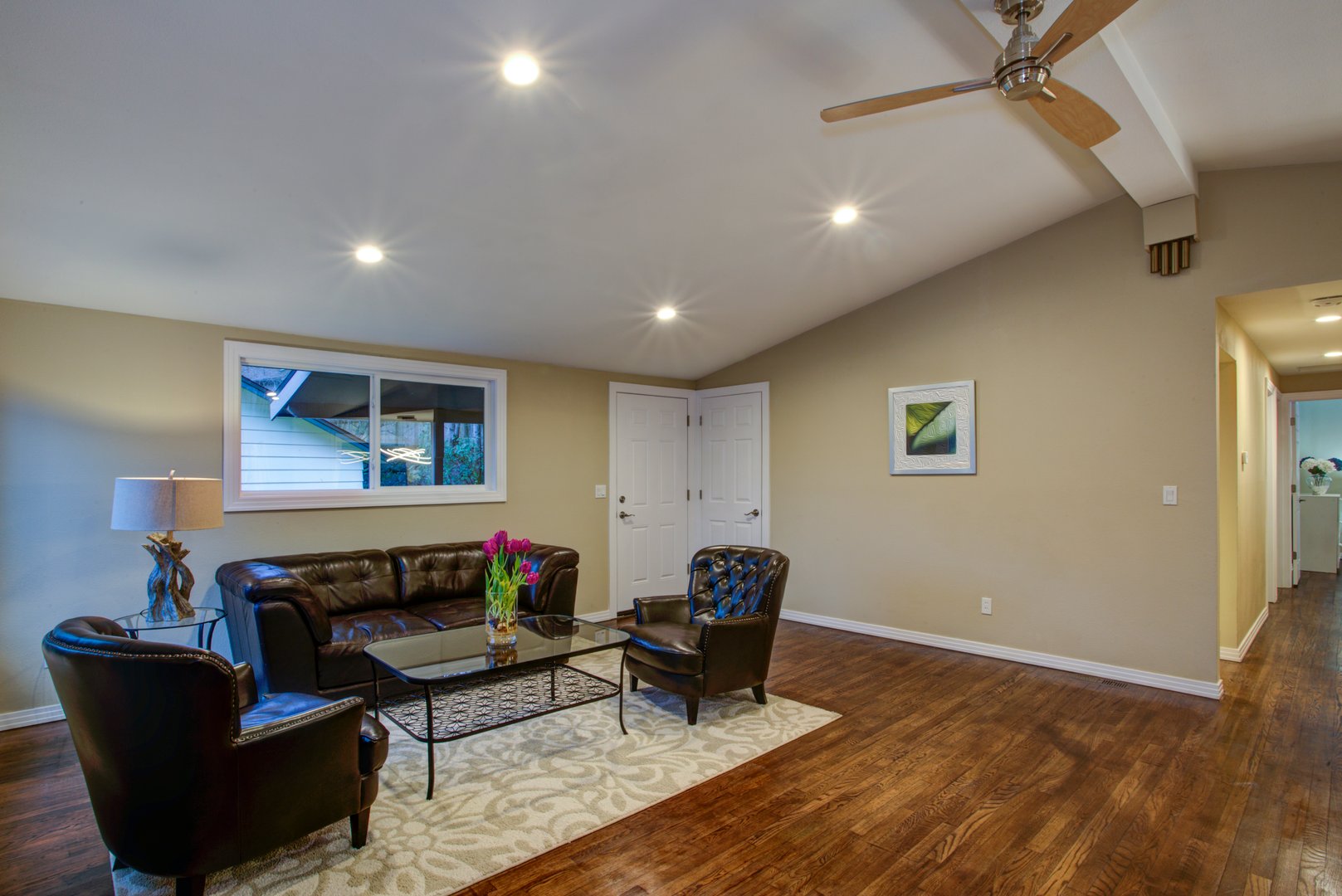 Luxury great room design with open floor plan: vaulted ceiling, shiny hardwood floor, stone wall fireplace, black leather armchairs.