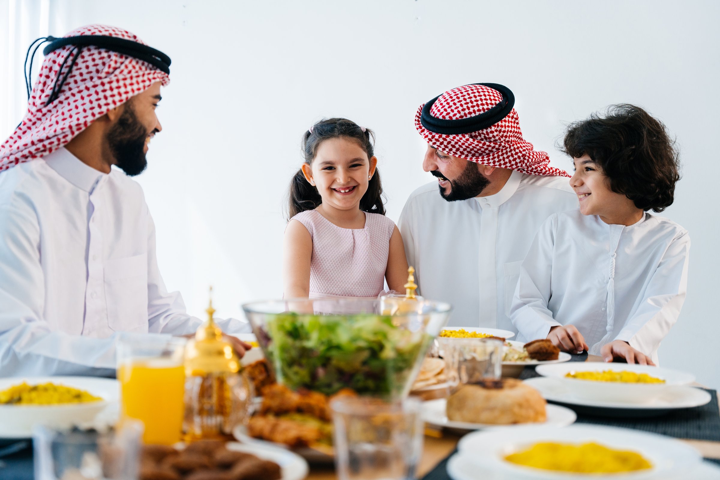 Happy arab family wearing saudi arabia clothing spending time together at home during dinner - Middle-eastern saudi parents and children celebrating ramadan after day fasting