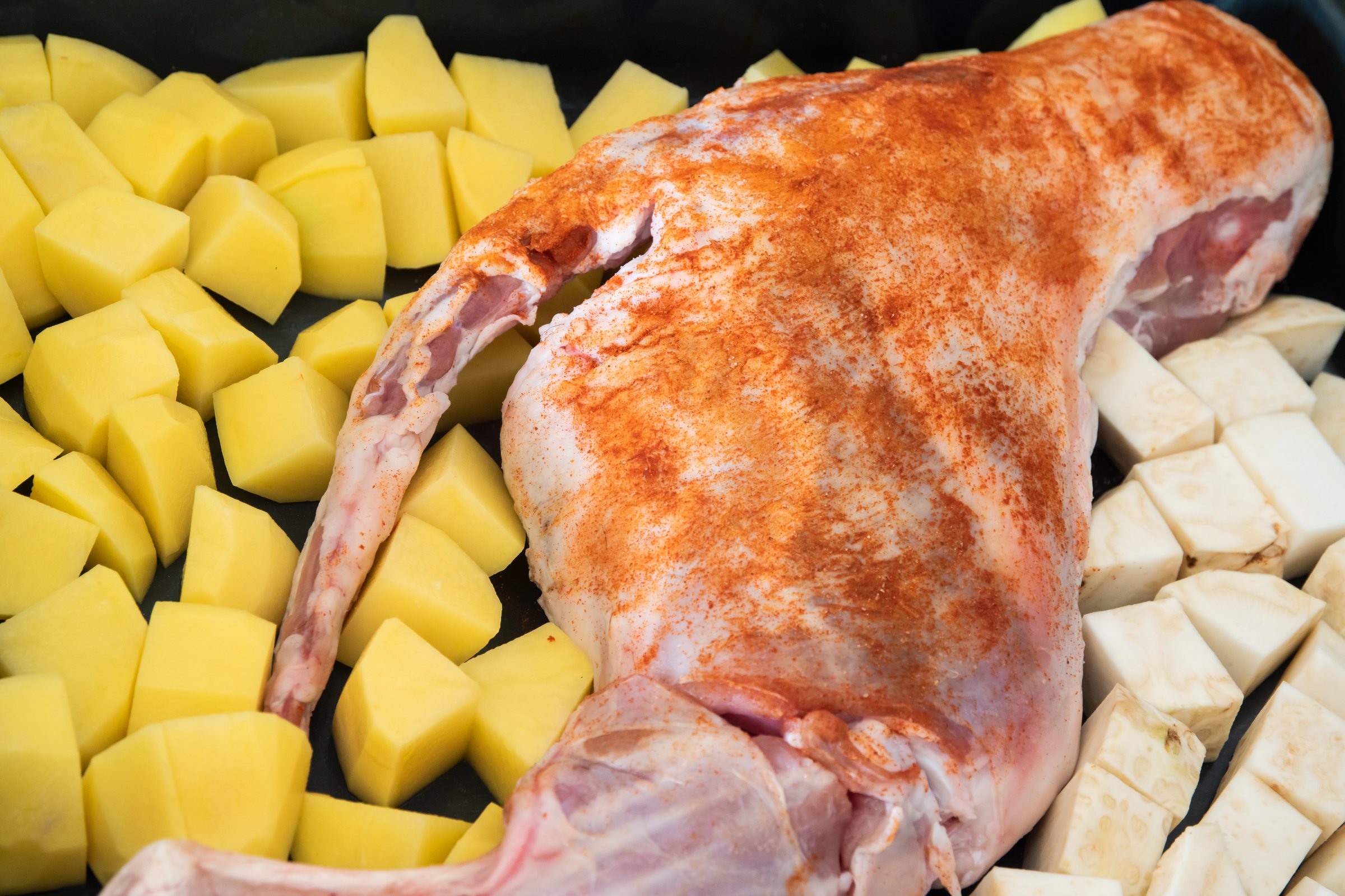 Prepared for cooking in the oven raw leg of lamb with chopped potatoes and celery