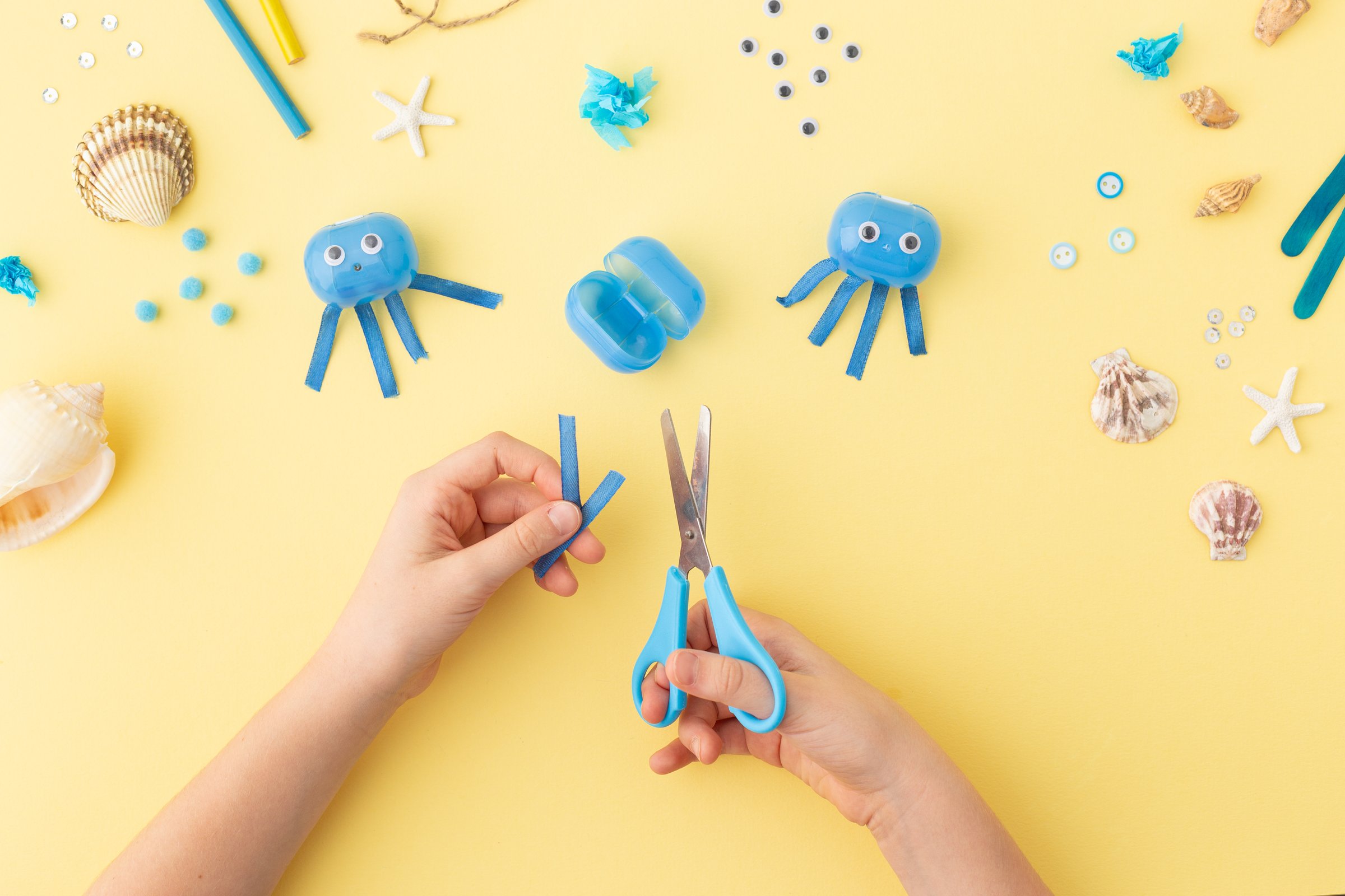 Adorable jellyfish made from plastic blue egg, Kids craft at home or kindergarten. Hands making DIY summer crafting with children. Ocean's day. High quality photo