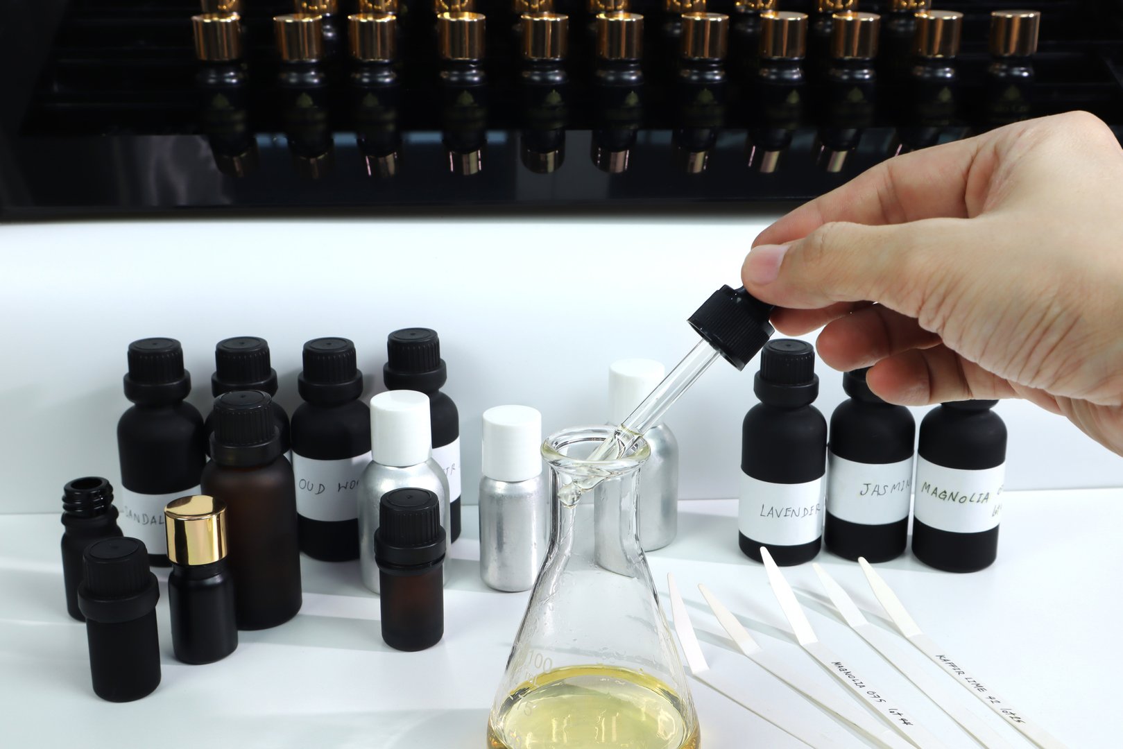 chemical beaker , flask is on white table with blotting paper , fragrance bottle and essential oil bottle are used to blend the nice scent for making perfume and candle by perfumer in the laboratory of home fragrant factory