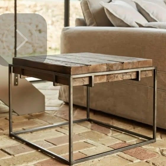 A rustic wooden coffee table with a metal frame placed on a brick floor beside a beige sofa with cushions.