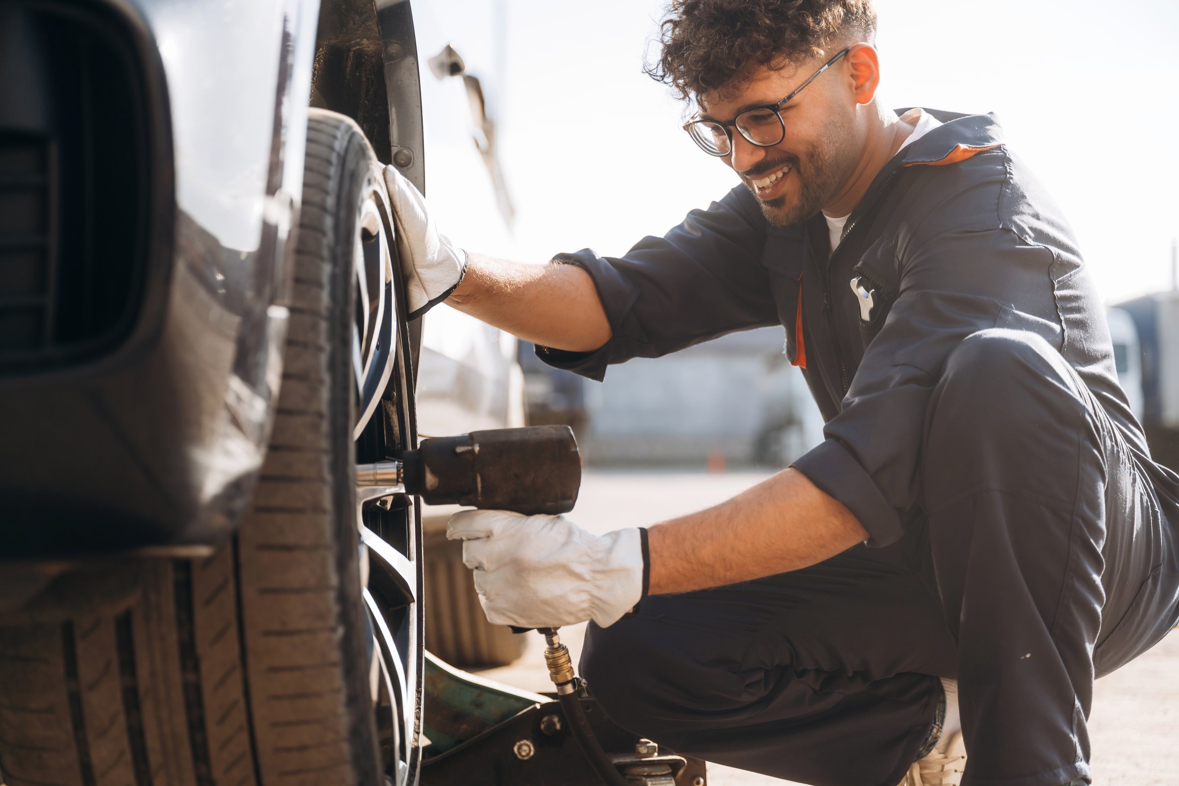 Screwdriver in hand. Mechanic is with the car outdoors.