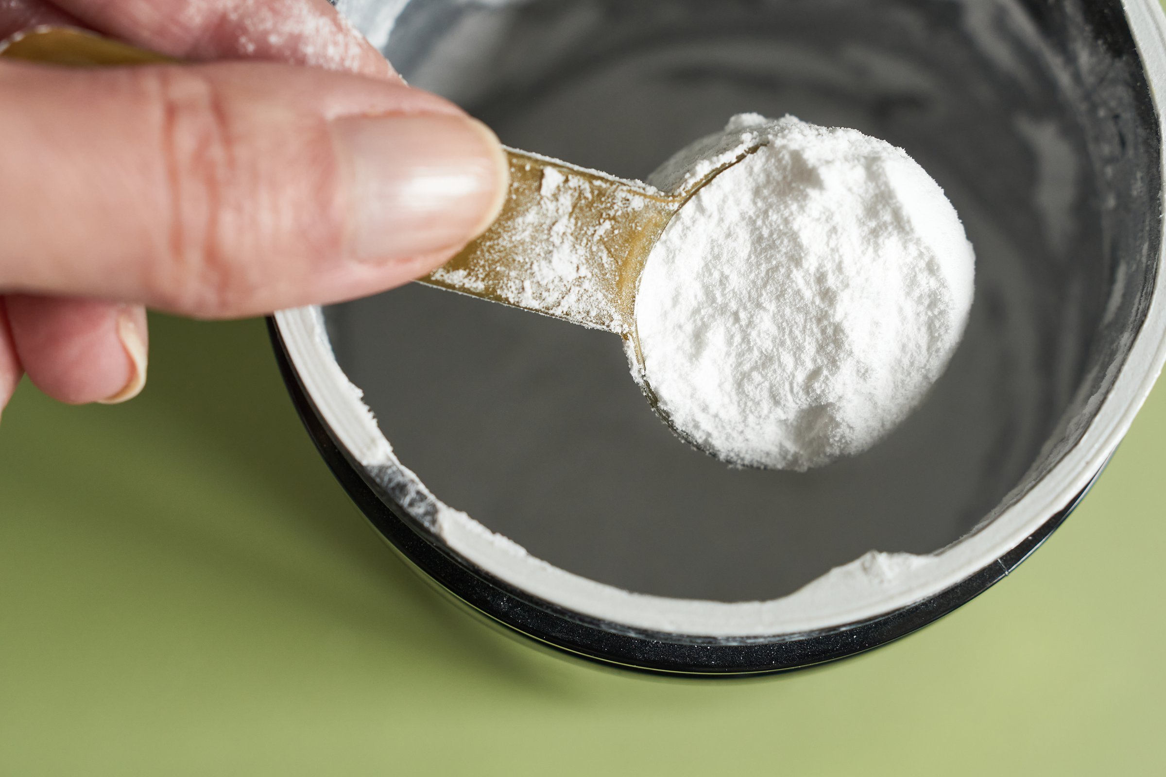 A spoonful of creatine powder in a metal jar, close-up. Female athlete taking creatine from the jar.
