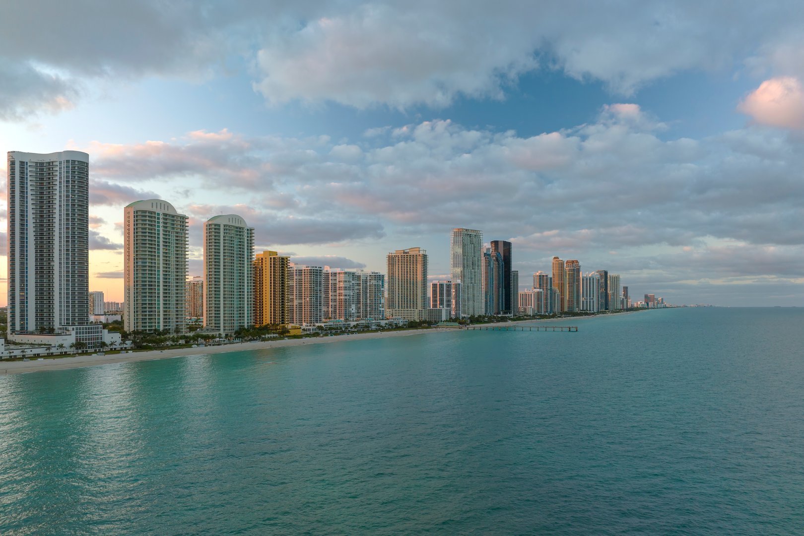 Expensive highrise hotels and condos over sandy beachfront on Atlantic ocean shore in Sunny Isles Beach city at sunset. American tourism infrastructure in southern Florida.