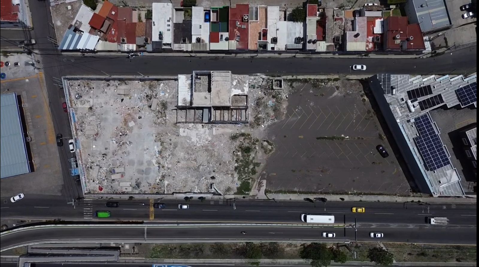 Aerial view of an urban area with a construction site, road with vehicles, and residential buildings in the background.