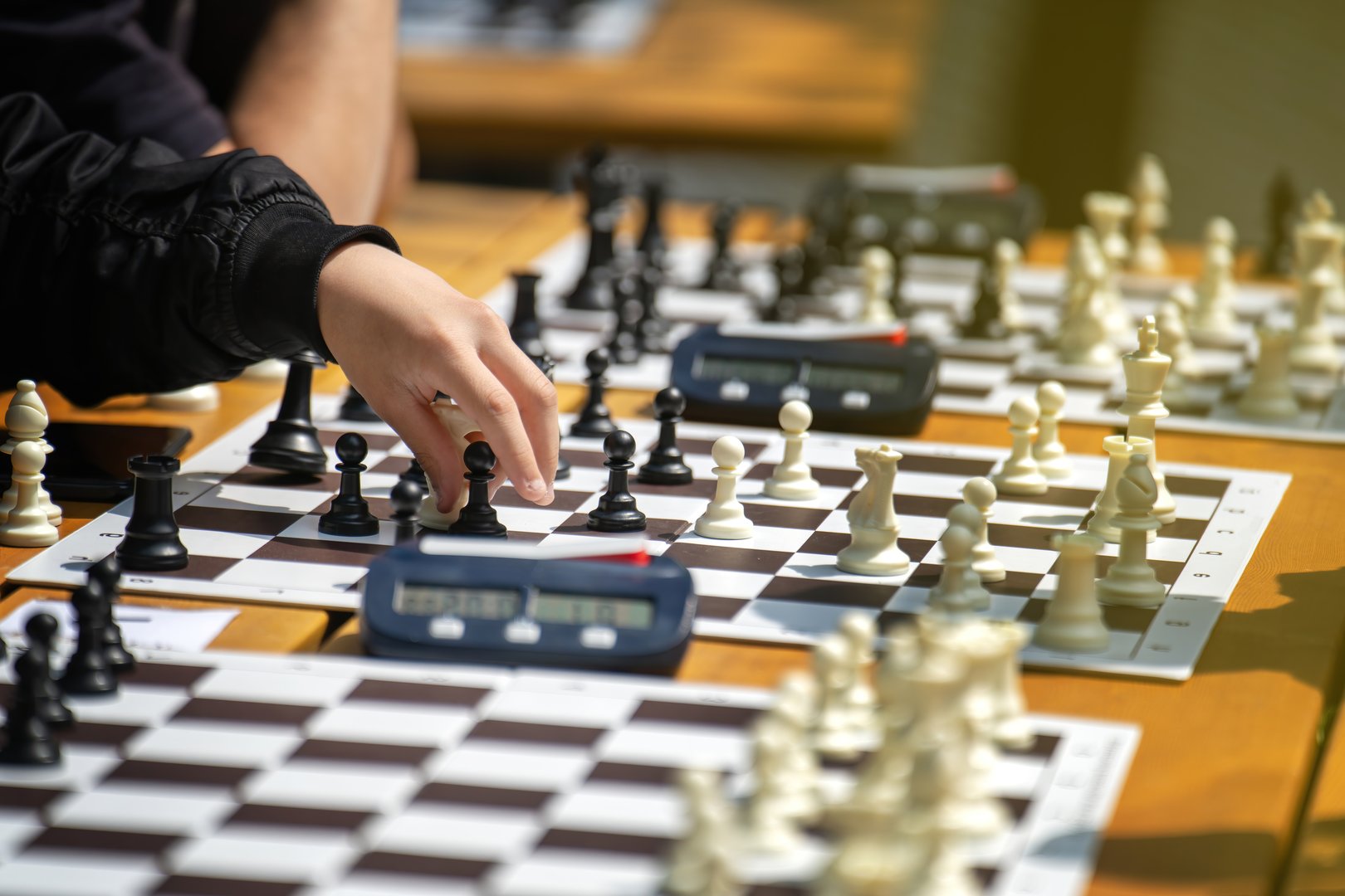 People's hands moving chess pieces on sunlit boards during an outdoor park game on a summer day. People's hands moving chess pieces on sunlit boards during an outdoor park game on a summer day.