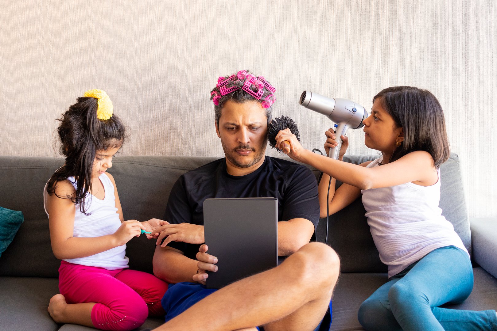 Pretty daughters are painting the nails and combing the hair of their handsome young father