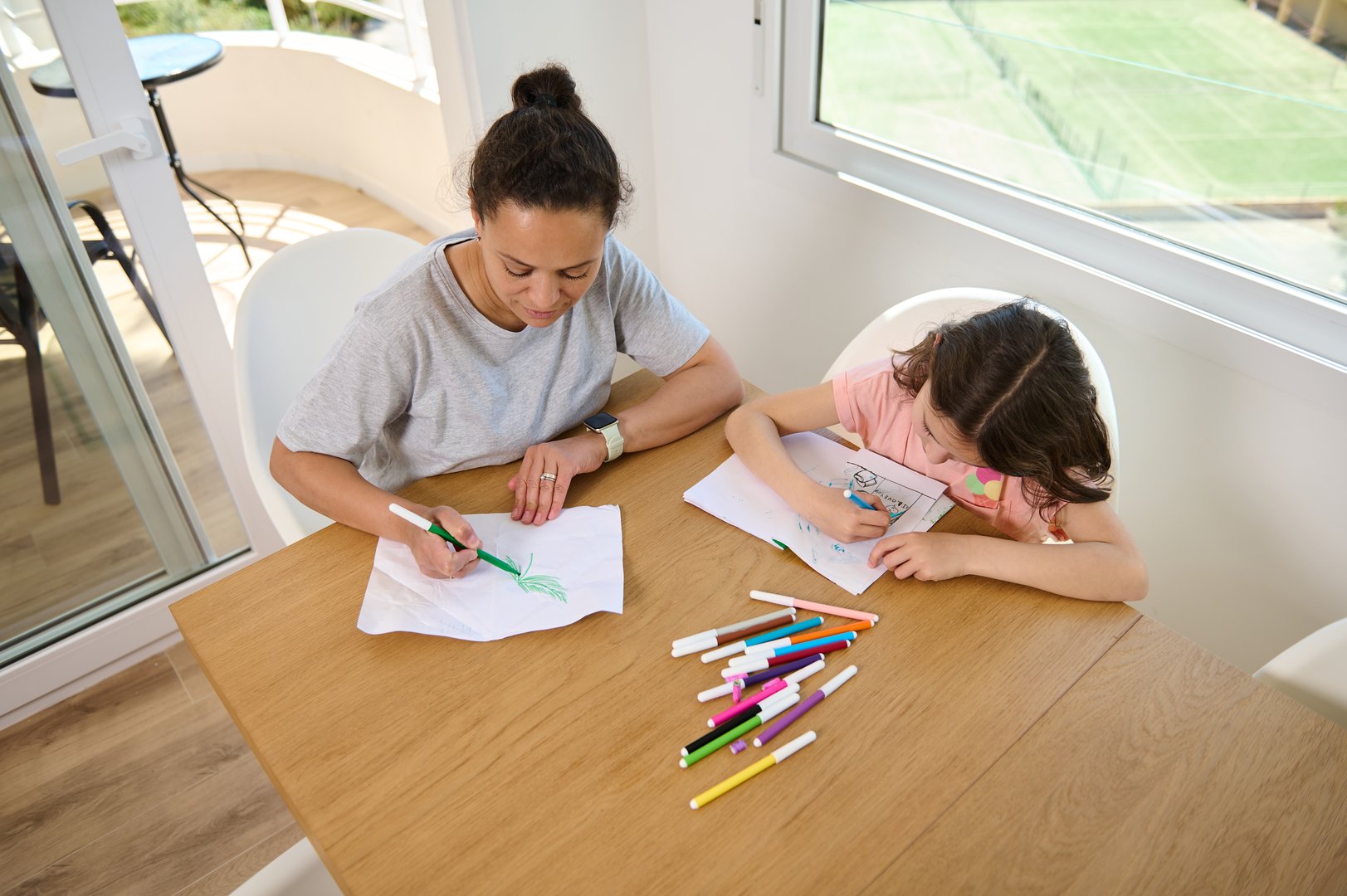 A mother and daughter spending quality time drawing and coloring at a table surrounded by markers.