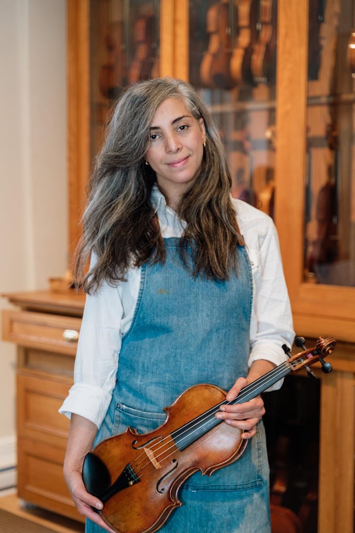 Skilled luthier carefully polishing wooden violin surface, buffing intricate details with soft cloth in sunlit professional workshop, highlighting craftsmanship of musical instrument restoration