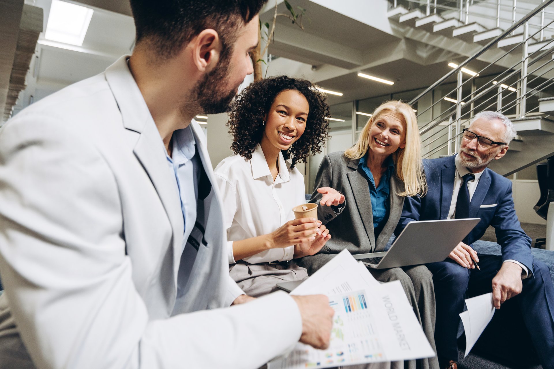 Multi-ethnic business team engaging in an informal meeting, reviewing marketing data and discussing reports in a modern office lobby, fostering collaboration and innovative ideas. Business concept
