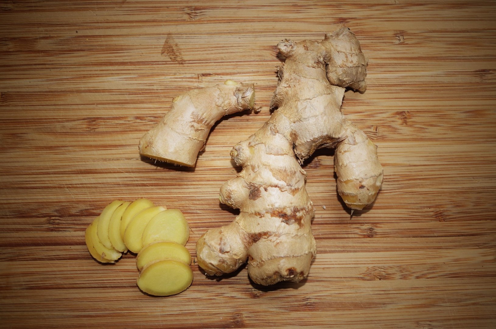 Whole ginger root and sliced pieces on a wooden cutting board.