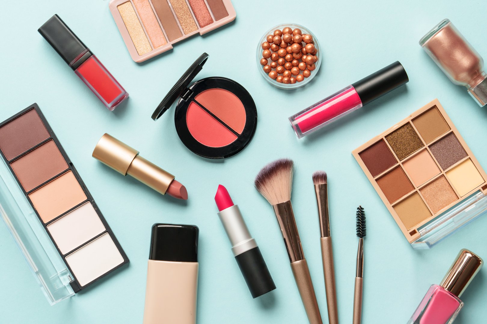 Beauty products on blue background. Cosmetic palette, brushes, cream and lipsticks. Top view.