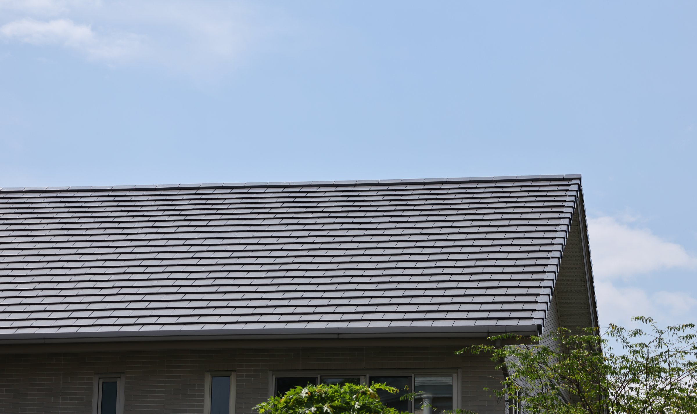 A house with a grey roof and a blue sky in the background. The roof is slanted and has a few windows
