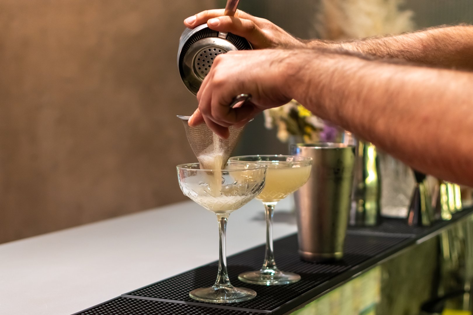 Bartender expertly straining cocktail into elegant coupe glasses