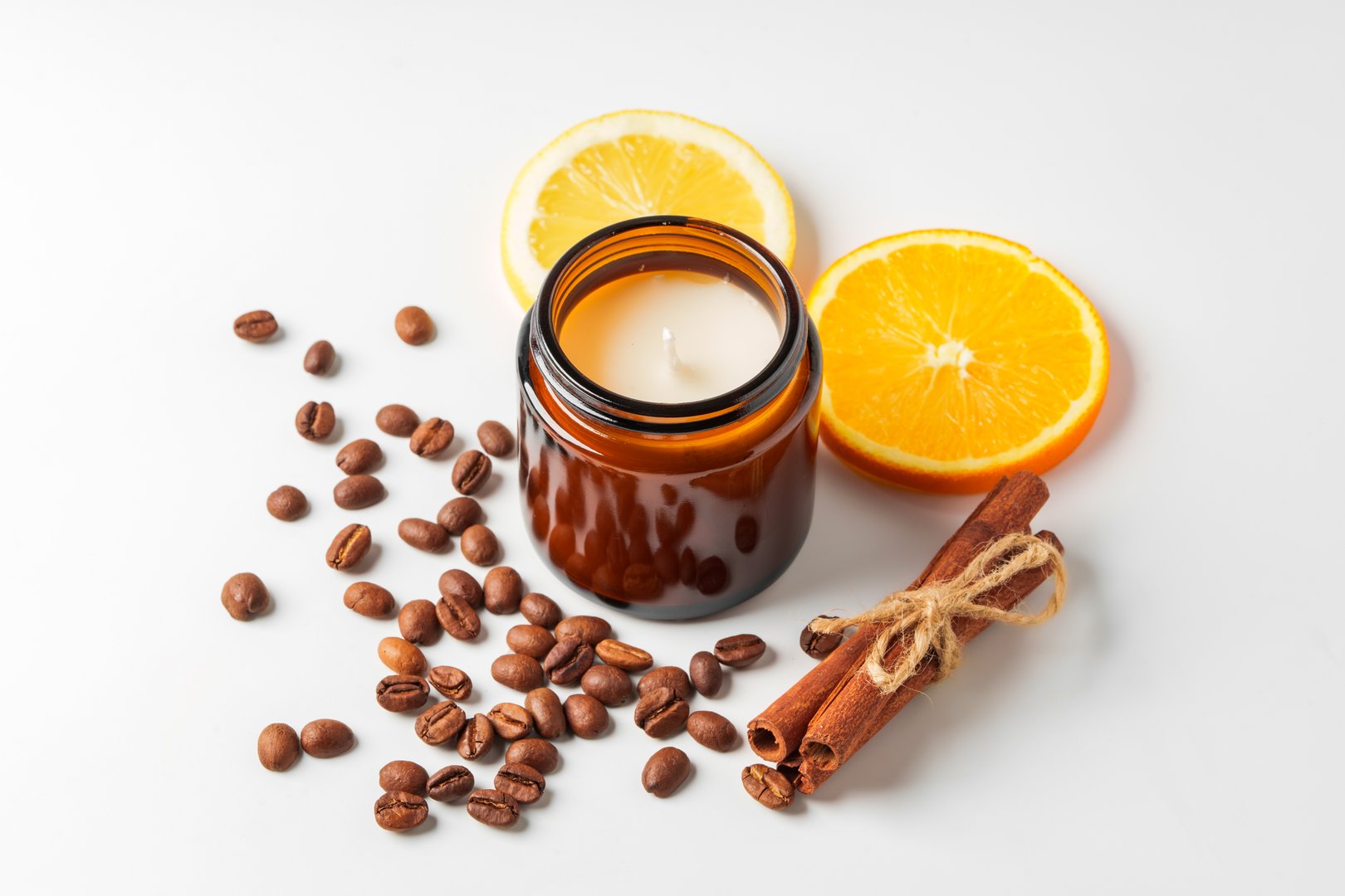 Aromatic candle, coffee beans, orange slices, and cinnamon sticks arranged on a white background close up