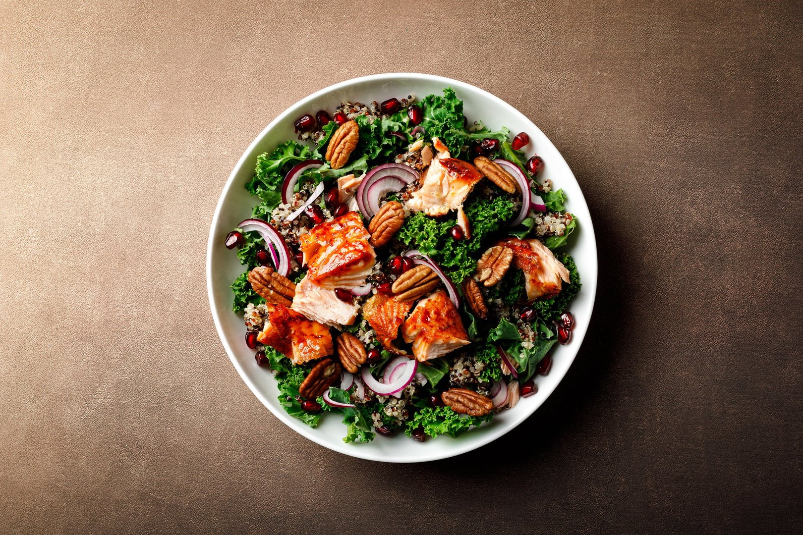 Salmon superfood salad with grilled fish, kale, quinoa, pecan nuts, red onion and pomegranate. Top view