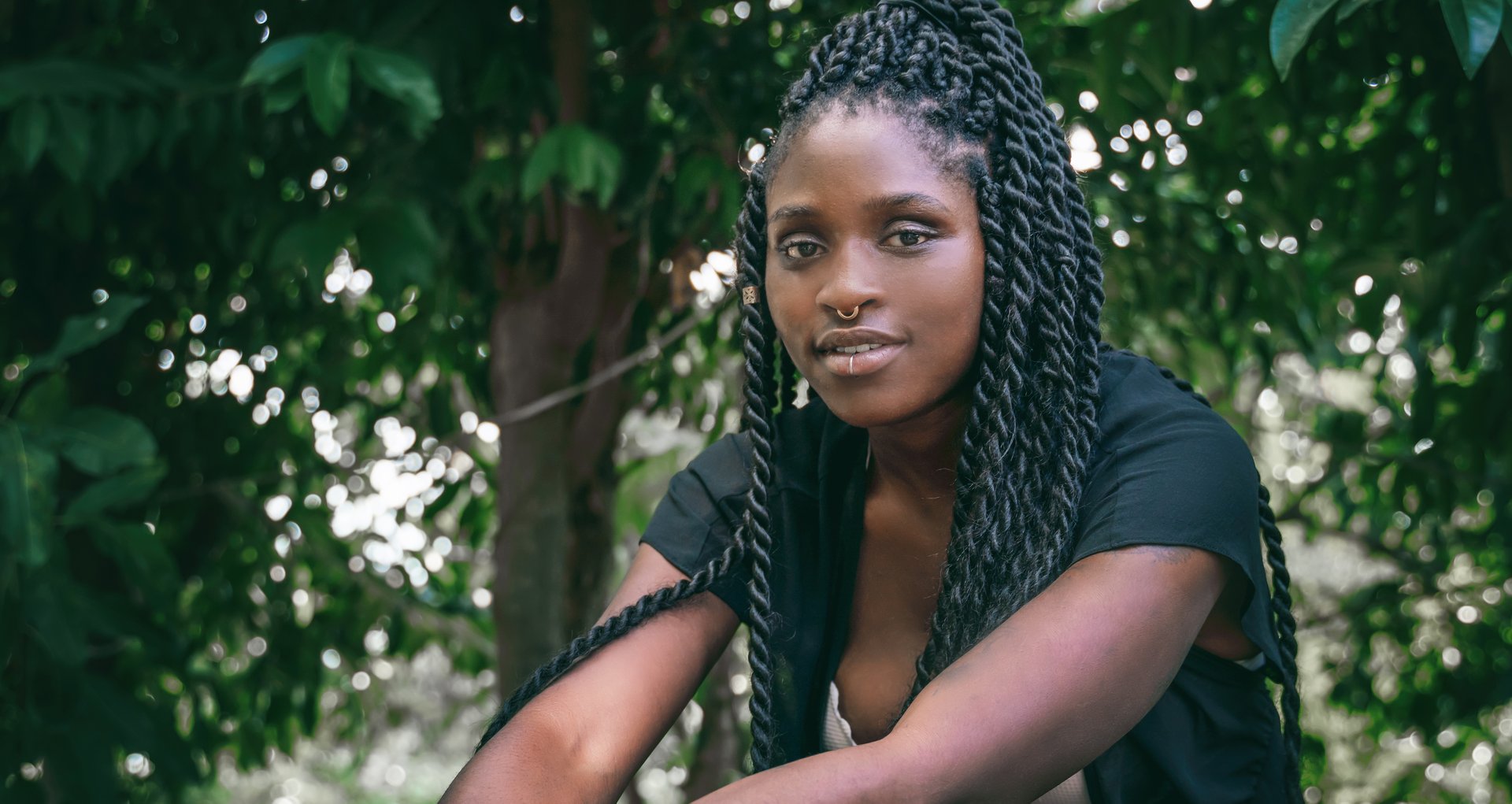 Charming beautiful young african american woman girl with black pigtails with piercings on her face, portrait in a tropical garden