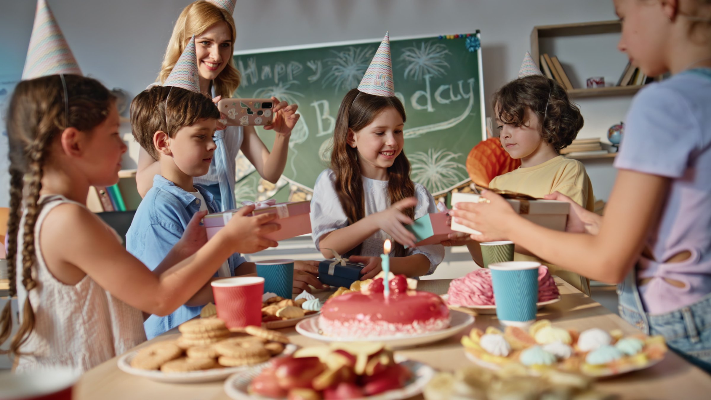 Kids celebrating birthday in classroom. Happy schoolgirl receiving gifts from group classmates