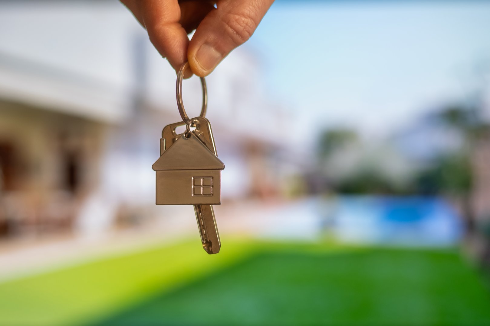 Real estate agent holding house keys with a new property in the background, representing the concept of homeownership, investment, and mortgage