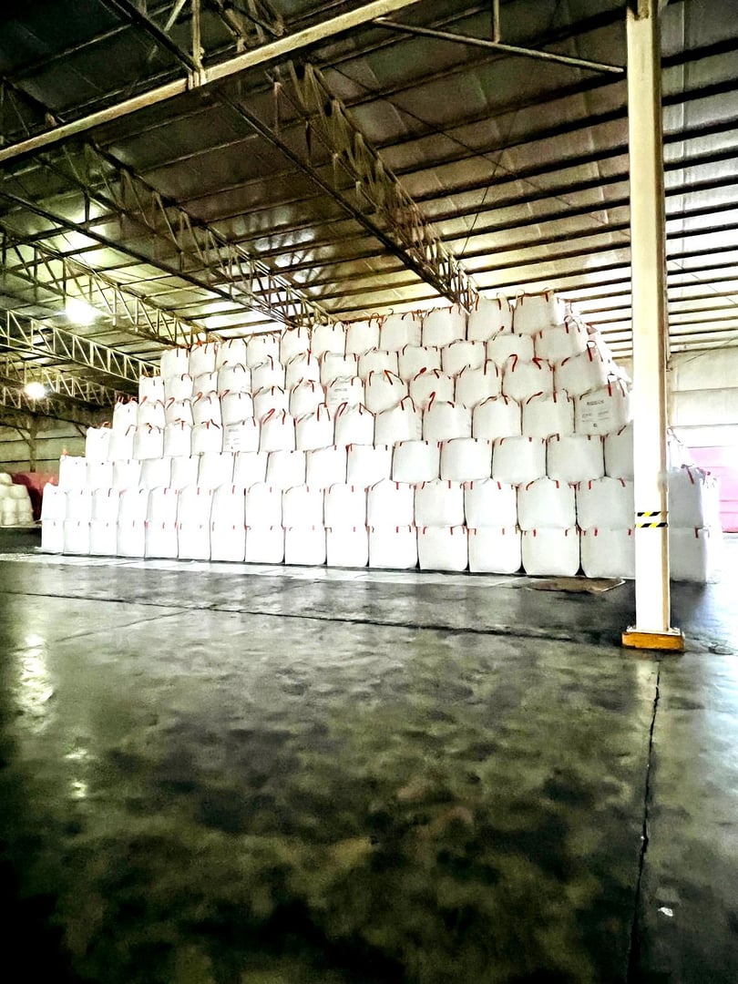 Large stacks of white storage bags piled in a warehouse with a metal roof and concrete floor.