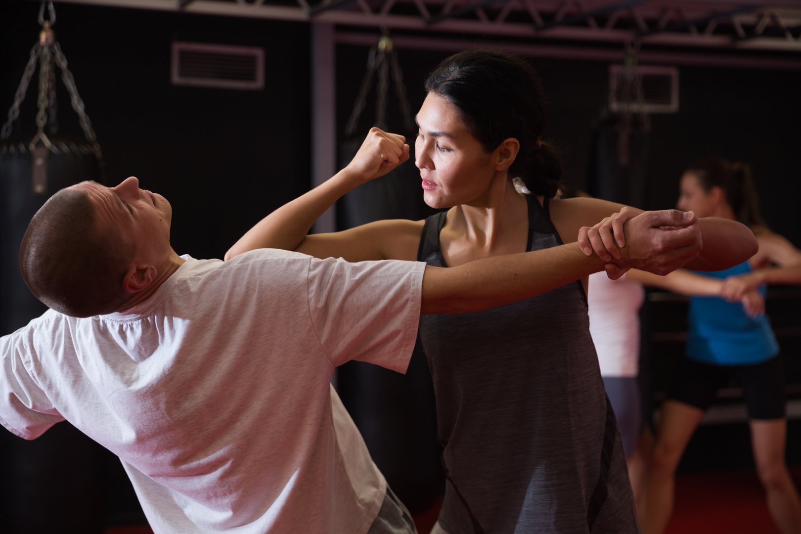 Asian woman training elbow strike with caucasian man in gym during self-defence training