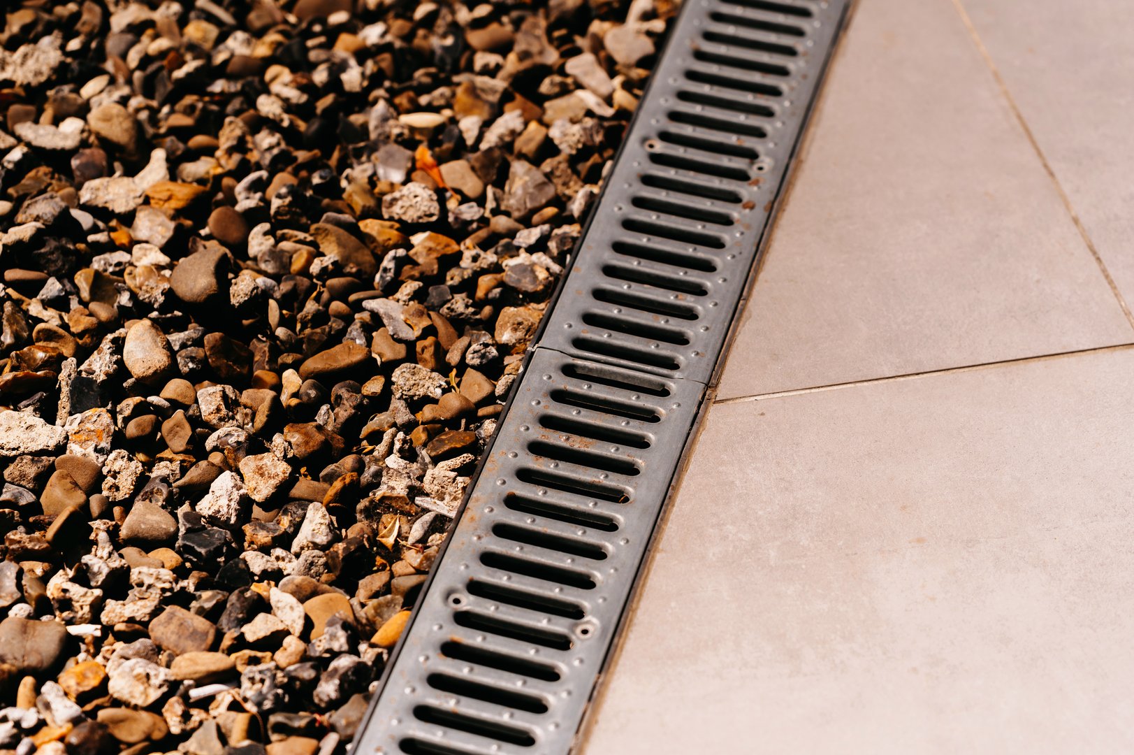 An impeccably clean drainage grate situated next to beautifully arranged decorative gravel and tiled flooring