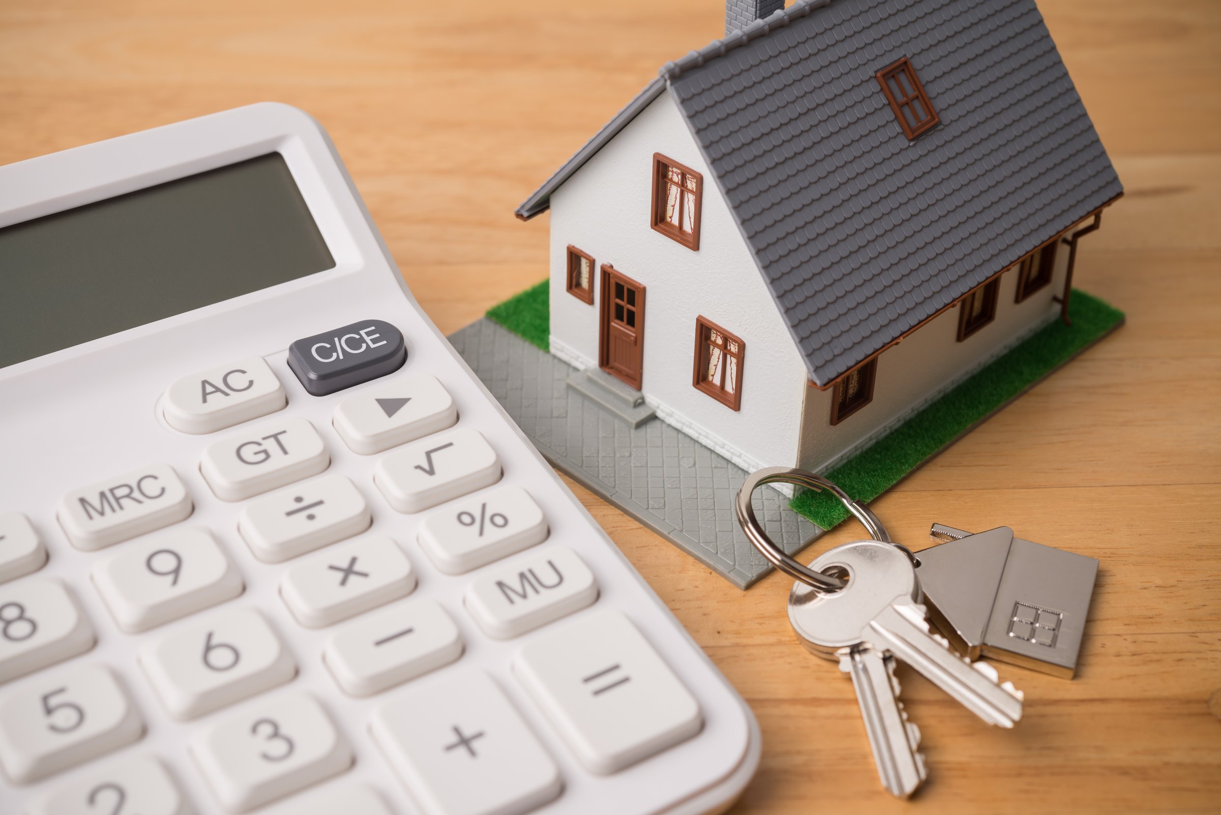 House model, key and white calculator on wooden table background. Mortgage loan for buying home or real estate property, money saving plan, money risk management in financial banking concept.