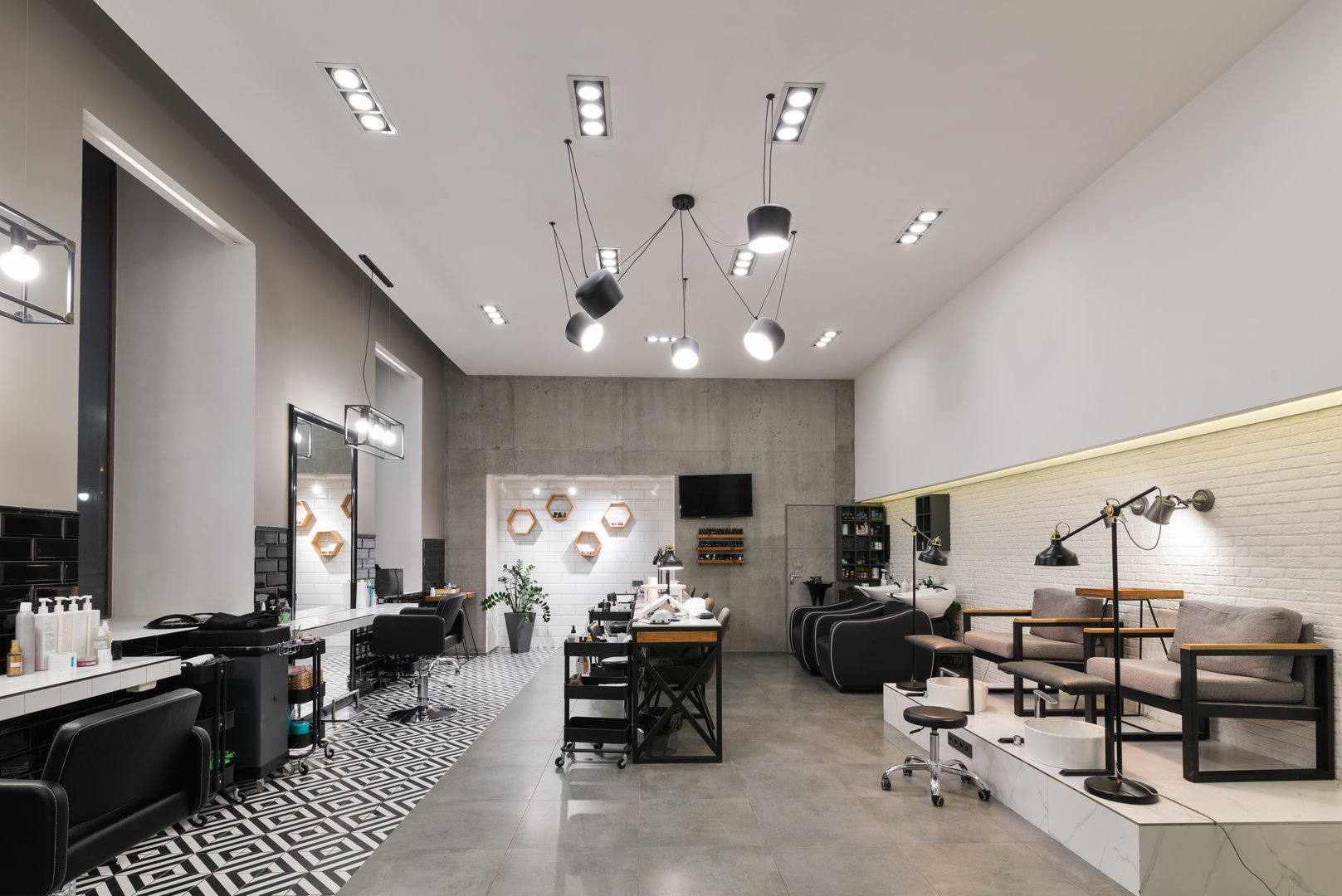 Modern interior of the beauty salon which consist of nail salon and barbershop with black lamps and concrete wall. Mirrors, chairs, backwashes and other equipment are in the salon.