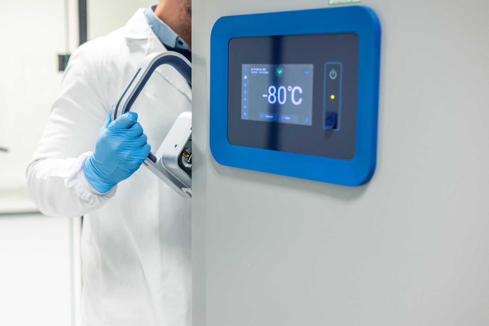 Scientist in a lab coat and gloves opening an ultra-low temperature freezer in a scientific laboratory, ensuring the preservation of samples stored at -80°C for ongoing research