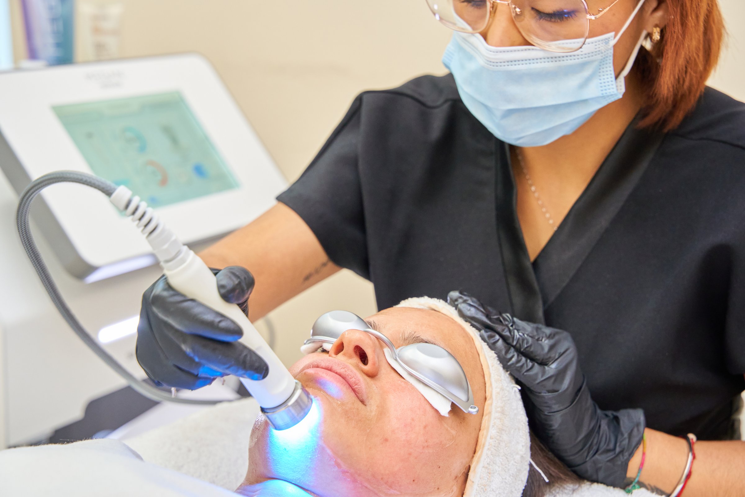 A woman is getting a facial treatment with a machine. The woman is wearing a mask and gloves