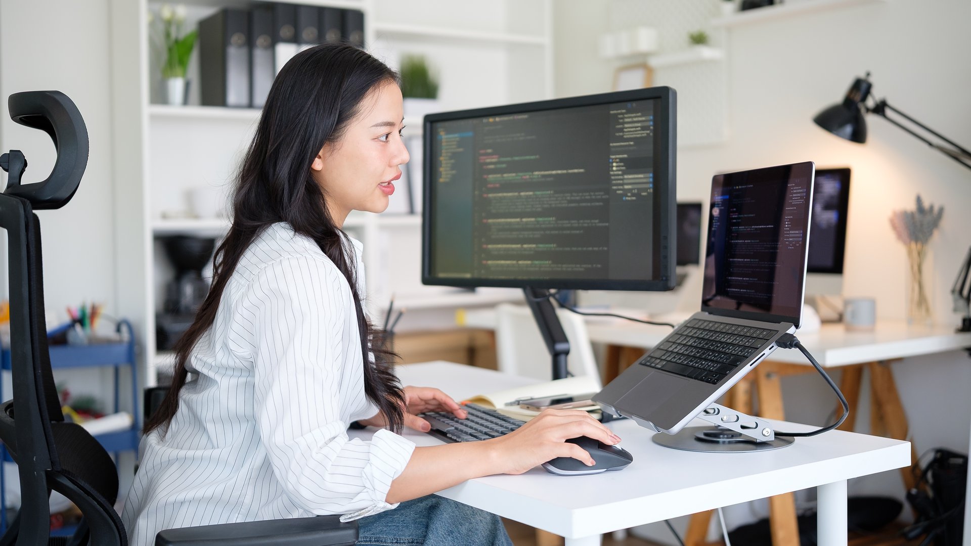 Asian woman software engineer coding on multiple screens.