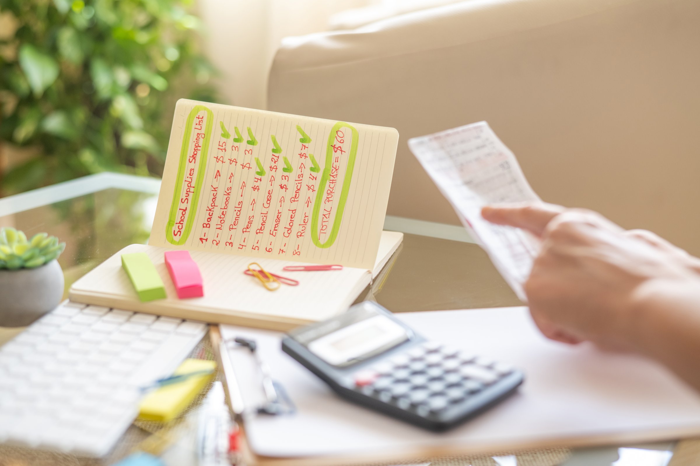 Parent is using a calculator and checking a receipt while reviewing a back to school shopping list for school supplies, calculating expenses and managing the family budget